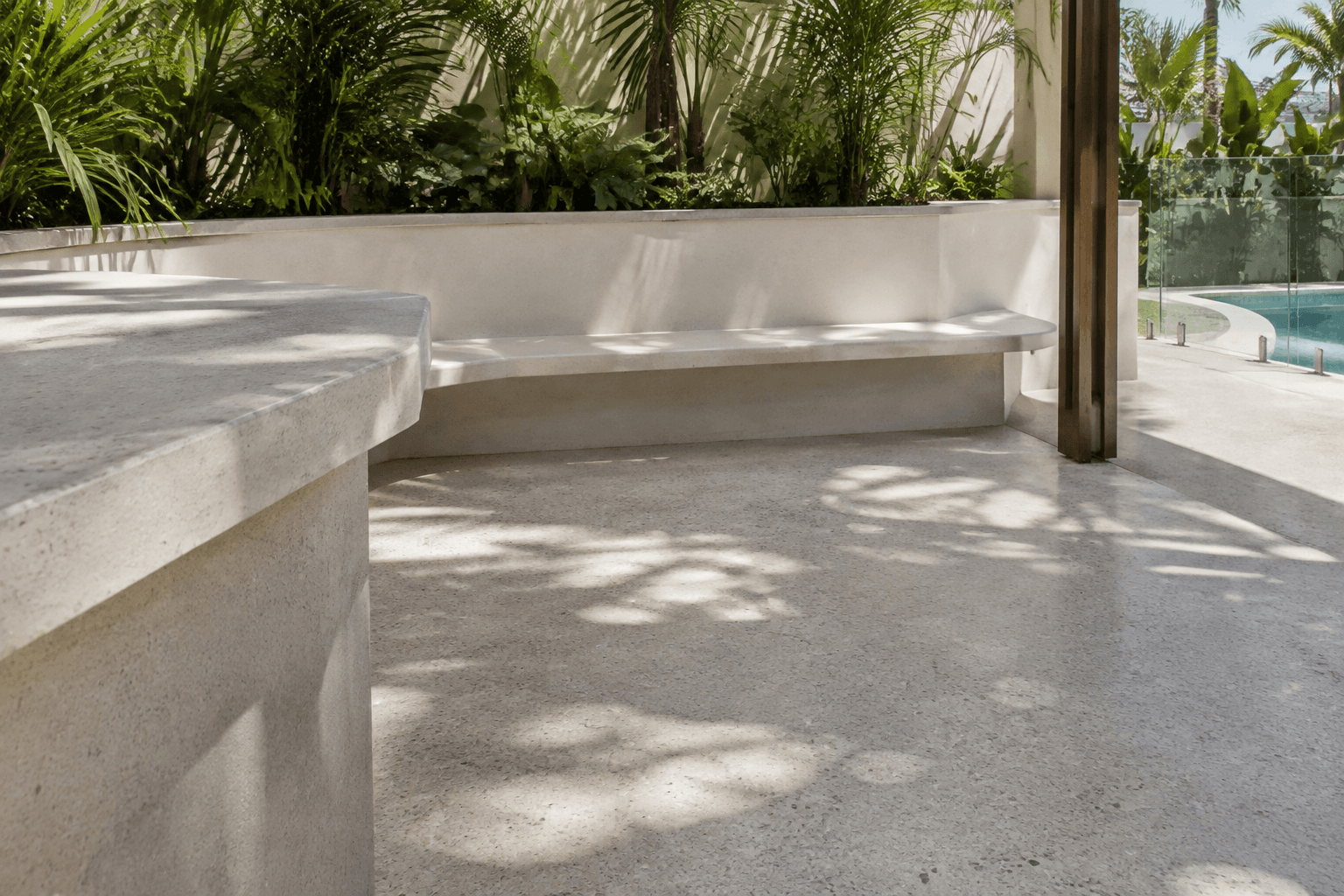 Pale concrete poolside terrace with curved seating and coastal planting